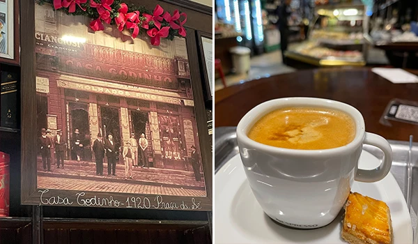 Imagem de um quadro antigo de 1920 na parede de um local com copo de café com leite e um bolo de pedaço. O quadro mostra uma cena histórica com pessoas na rua, destacando a fachada de uma loja antiga.