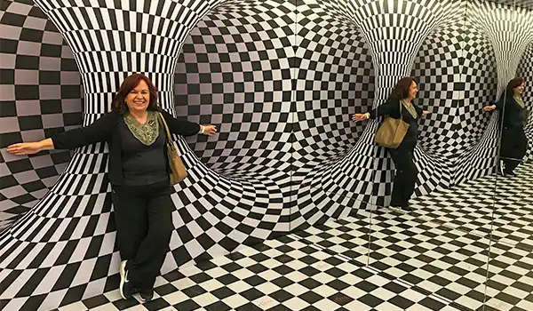 Deusa Rodrigues posando dentro de uma instalação artística de parede e piso com padrão de ilusão de ótica preto e branco, criando um efeito tridimensional
