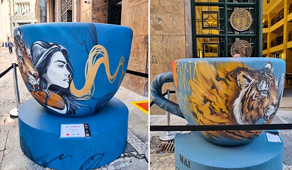 Imagem de uma escultura de balde com arte urbana que apresenta uma mulher com cabelo laranja e um tigre, ambas com detalhes realistas em um ambiente urbano moderno.