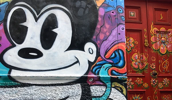 Grafite colorido com personagem de desenho animado e porta decorada com flores e detalhes artísticos na parede.