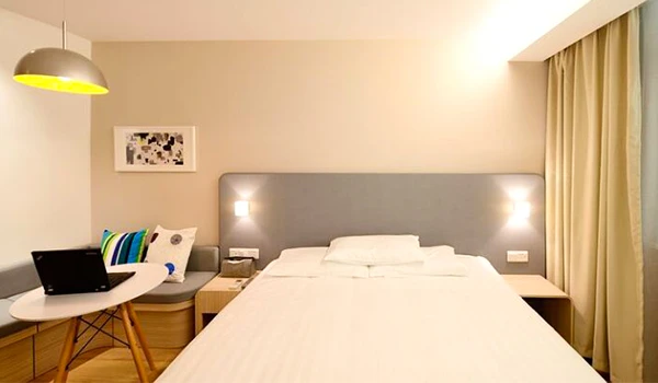 Quarto de hotel moderno e aconchegante com cama de casal, iluminação suave, decoração minimalista com quadro na parede e uma escrivaninha com laptop, ideal para relaxar ou trabalhar.