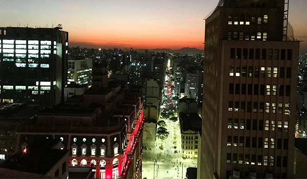 Por do sol no Farol Santander na cidade de São Paulo, com ruas iluminadas e prédios altos em destaque, oferecendo uma perspectiva urbana vibrante.