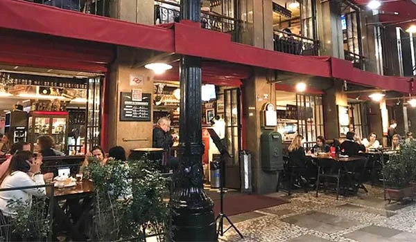 Ambiente de restaurante ao ar livre em uma noite com várias pessoas desfrutando de uma refeição, luzes acolhedoras e decoração elegante na cidade