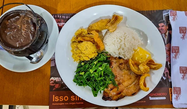 Prato tradicional de comida brasileira com arroz, feijão, carne, salada verde e banana, acompanhado de refrigerante em um restaurante.