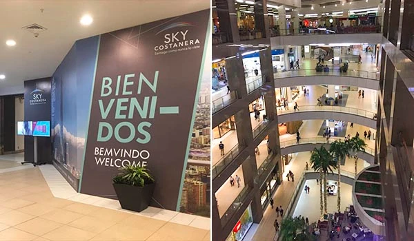 Interior de shopping center com grande sinal de boas-vindas na parede, e múltiplos níveis com lojas e visitantes, destacando o ambiente comercial e de lazer.