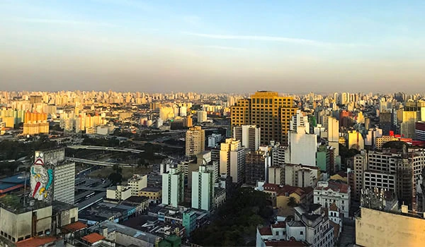 Vista panorâmica de São Paulo ao entardecer, com prédios altos, ruas movimentadas e céu claro, destacando a beleza urbana da cidade.