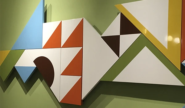 Composição abstrata com formas geométricas em papel nas cores azul, verde, branco e laranja, com triângulos e quadrados sobre fundo verde, estilo arte moderna.