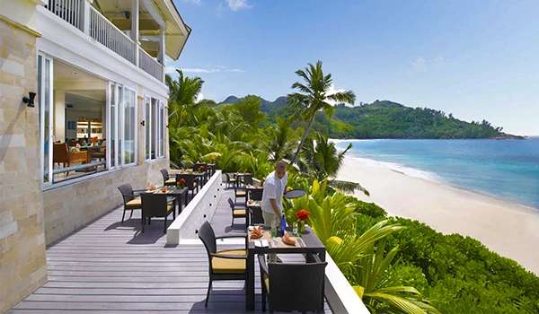 Prato de café da manhã no terraço de um hotel à beira-mar em um ambiente tropical com vista para o oceano e vegetação exuberante.