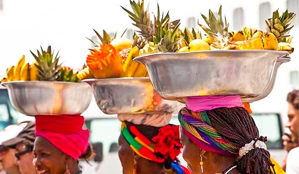 Mulheres colombianas carregando cestos de abacaxis na cabeça durante um evento cultural, usando turbantes coloridos, em uma celebração ao ar livre. Cultura e as danças da América do Sul.