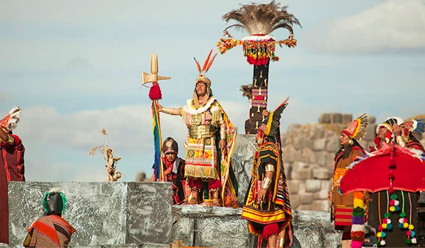 Cena de celebração indígena tradicional com pessoas vestidas com roupas coloridas e adornos cerimoniais, com fundo de céu azul e estruturas antigas. Cultura e as danças da América do Sul.