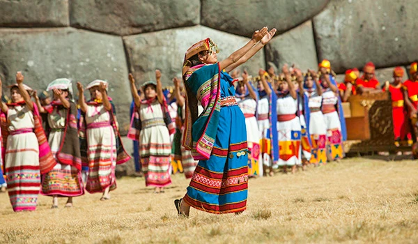 Dança tradicional indígena da Festa Inti Raymi no Peru, com participantes vestindo roupas coloridas e acessórios típicos, em cidade com árvores e arquitetura colonial ao fundo. Cultura e as danças da América do Sul.
