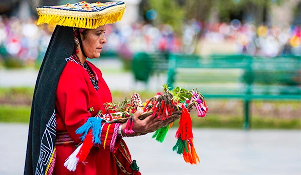 Mulher indígena vestida com traje tradicional colorido durante celebração cultural, segurando um espeto com alimentos decorativos no Peru. cultura e as danças da América do Sul.