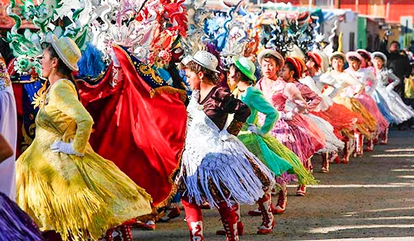 Grupo de pessoas participando de uma festa tradicional com roupas coloridas e dançando em uma rua durante o evento. Cultura e as danças da América do Sul.