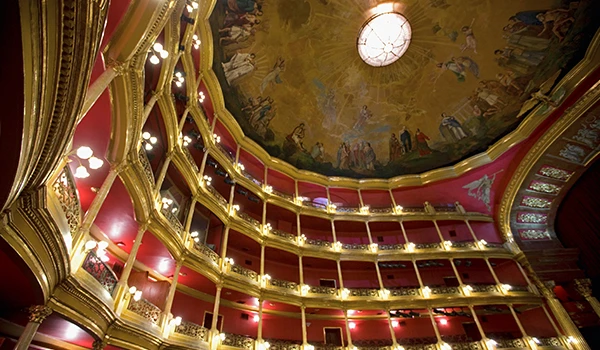 Imagem do interior de um teatro clássico com várias poltronas e caixas de camarote decoradas em estilo antigo com iluminação amarela e teto com pintura artística. O que fazer em Guadalajara.