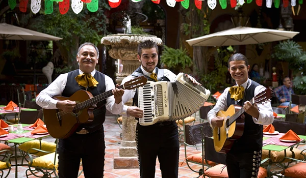 Trio de músicos tocando violão e acordeão em festa ao ar livre, decorada com bandeirinhas e garantindo animação e cultural local. O que fazer em Guadalajara.