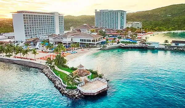 Vista aérea do complexo hoteleiro em um resort de praia com piscinas, áreas de descanso, edificações modernas e uma bela vista para o mar, ideal para Lua de Mel na Jamaica.