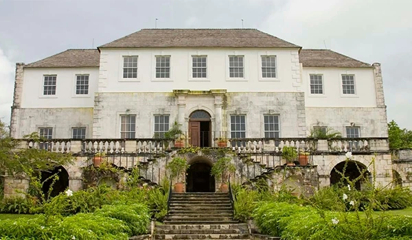 Luxuoso castelo antigo com jardins bem cuidados na frente, pôr do sol ao fundo, transmitindo elegância e história na arquitetura clássica.