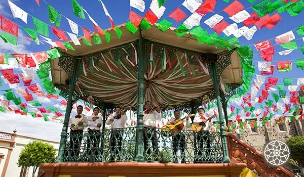 Celebração de festa junina com música ao vivo, bandeirinhas coloridas e uma decoração típica, destacando um palco ao ar livre com várias pessoas tocando violão.