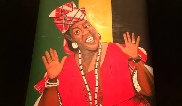 Imagem de uma mulher negra com expressão alegre, usando roupas tradicionais africanas e acessórios, representando cultura e identidade africana.