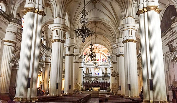 Interior de uma igreja com arquitetura clássica, pilastras altas e decoração elaborada, destacando um altar ao fundo com detalhes dourados e janelas com vitrais coloridos. O que fazer em Guadalajara.