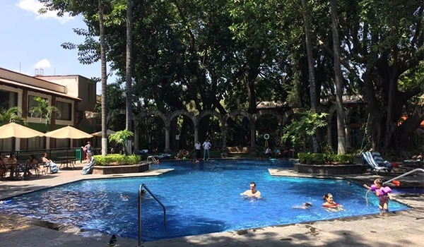 Piscina ao ar livre rodeada por árvores e pessoas aproveitando o dia de lazer em um ambiente tranquilo e agradável.