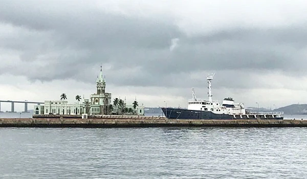 Imagem da Ilha Fiscal no Rio de Janeiro com um navio atracado ao píer, sob céu nublado e águas calmas, símbolo turístico e histórico da cidade.