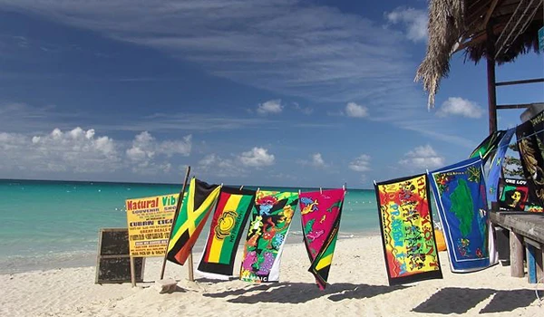 Bandeiras de beach towels coloridas em uma praia com mar azul e céu claro ao fundo, refletindo um ambiente tropical e relaxante. Jamaica praias.