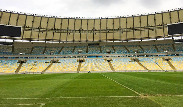 Estádio de futebol vazio com gramado bem cuidado e arquibancadas coloridas, preparado para uma partida de futebol.