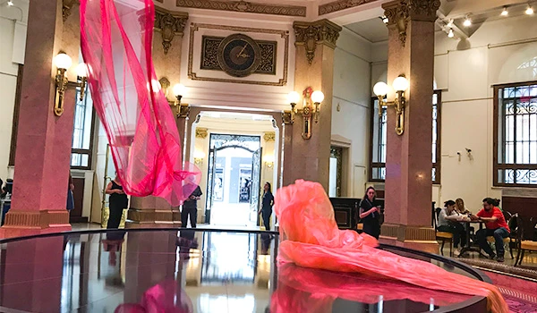 Arte contemporânea com tecidos rosa em um ambiente de pé direito alto, paredes decoradas, iluminação elegante e pessoas observando na sala de exposições.  Centro Cultural BB.