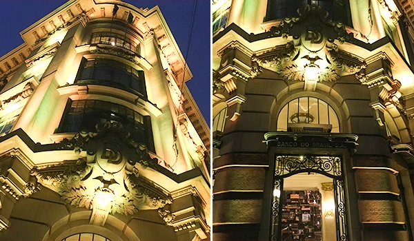 Edifício histórico iluminado à noite com fachada ornamentada e detalhes arquitetônicos clássicos, destacando-se pelo seu estilo antigo e iluminado.