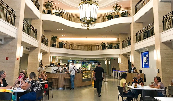 Interior da cafeteria com várias mesas, clientes aproveitando refeições, iluminação aconchegante e decoração elegante.