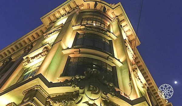 Fachada de um edifício antigo bem iluminado à noite, com detalhes arquitetônicos elegantes e janelas grandes, na cidade de São Paulo.