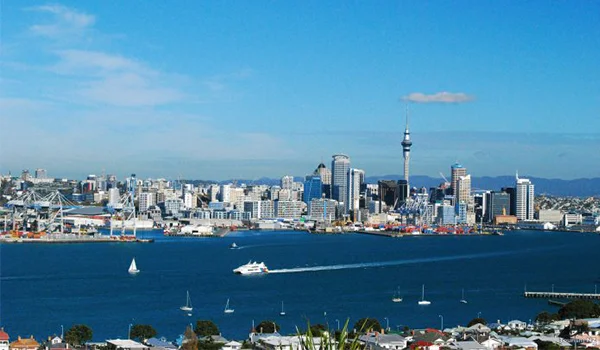 Foto da cidade de Auckland na Nova Zelândia onde se observar o mar com barcos e muitos prédios na terra.