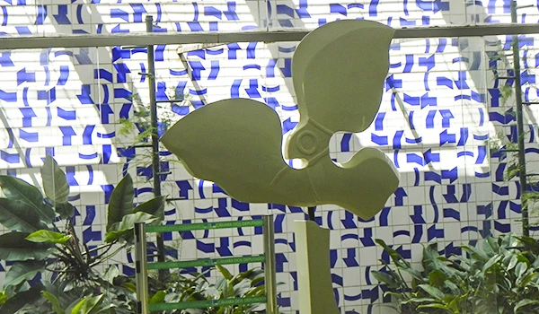 Escultura moderna rodeada por plantas e com fundo de azulejos decorativos em padrão azul e branco.