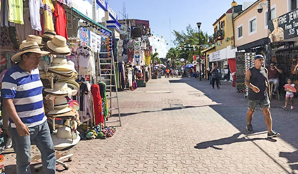 Rua de comércio ao ar livre no centro de uma cidade movimentada, com lojas de roupas, acessórios e turistas caminhando