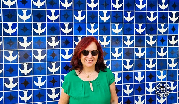 Deusa Rodrigues em frente a uma parede de azulejos azuis e brancos. A imagem destaca a beleza da arte urbana.
