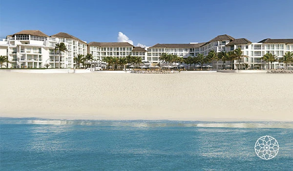 Vista da praia de areia branca com resorts de luxo ao fundo e mar calmo em um dia ensolarado, ideal para férias e lazer na areia.