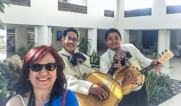 Deusa Rodrigues usando óculos escuros ao lado de dois homens tocando violões em ambiente interno