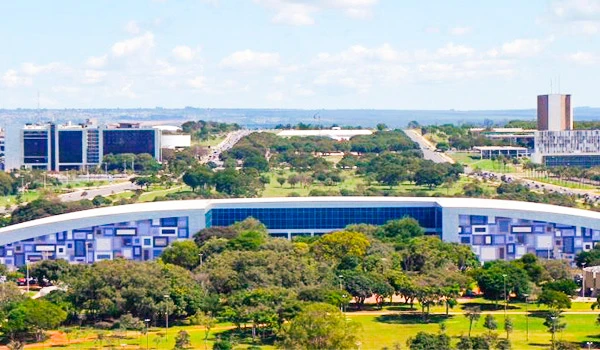 Imagem de um campus universitário com edifícios modernos, áreas verdes e céu claro, destacando a infraestrutura de uma instituição de ensino em uma cidade brasileira.