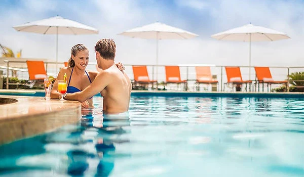 Casal aproveitando dia de lazer na piscina ao lado de espreguiçadeiras e guarda-sóis sob céu ensolarado, cenário ideal para relaxar e se divertir ao ar livre antes de casar em Cancun.