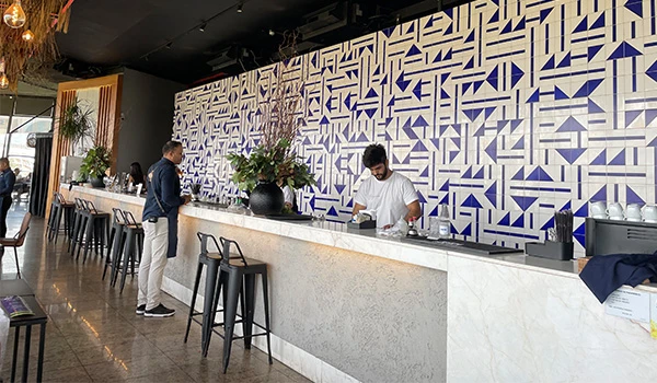 Bar moderno com decoração estilizada em azul e branco, com atendentes servindo clientes em um ambiente elegante e iluminado.