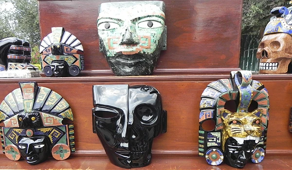 Várias máscaras de teatro e cultura indígena brasileira expostas em uma prateleira, destacando detalhes e cores vibrantes, incluindo máscaras negras, de pedra e com adornos diversos.