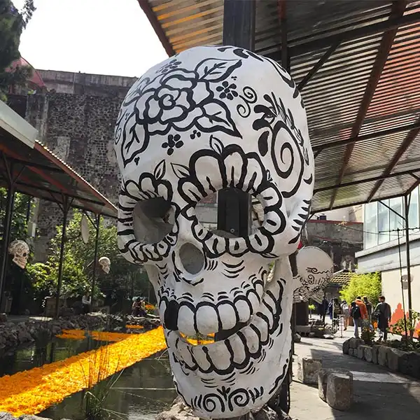 Escultura de caveira decorada com desenhos tradicionais em preto e branco, localizada ao ar livre sob uma cobertura de metal, em um ambiente de arte e cultura. Dia dos Mortos no México.