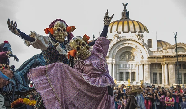 Dançarinos tradicionais de Dia dos Mortos em frente ao Palácio das Belas Artes na Cidade do México, vestindo roupas coloridas e máscaras de caveiras, celebrando a cultura mexicana.