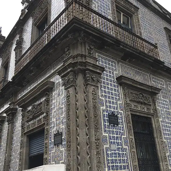 Imagem da fachada de um edifício antigo com detalhes ornamentais e azulejos azuis e brancos, destacando sua arquitetura clássica em estilo europeu.