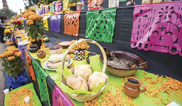 Celebração com altares tradicionais e comida típica mexicana, decorada com papel picado colorido e flores de cempasúchil durante o Día de los Muertos.