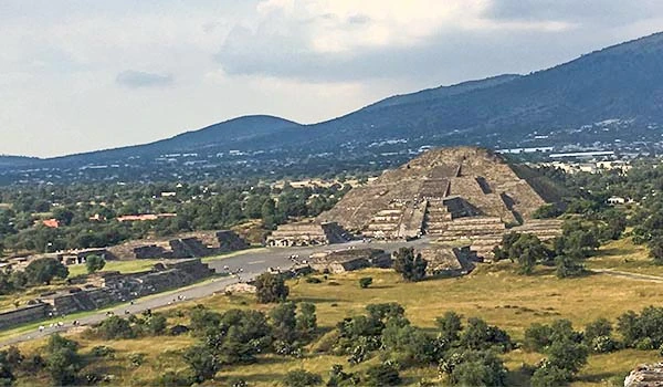 Vista Pirâmides do Sol e da Lua, cercada por vegetação e montanhas ao fundo.