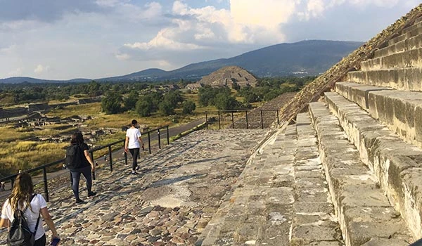 Turistas explorando as pirâmides de Teotihuacan no México, com a pirâmide ao fundo e uma trilha de pedra coberta de lanches. Pirâmides do Sol e da Lua.
