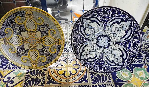 Conjunto de pratos de cerâmica decorativos com padrões em azul, branco e amarelo, típicos de Puebla.