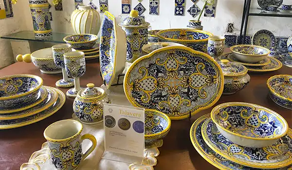 Conjunto de louças coloridas decoradas com detalhes em azul, branco e amarelo, incluindo pratos, bowls, canecas e garrafas, em uma loja de utensílios domésticos.